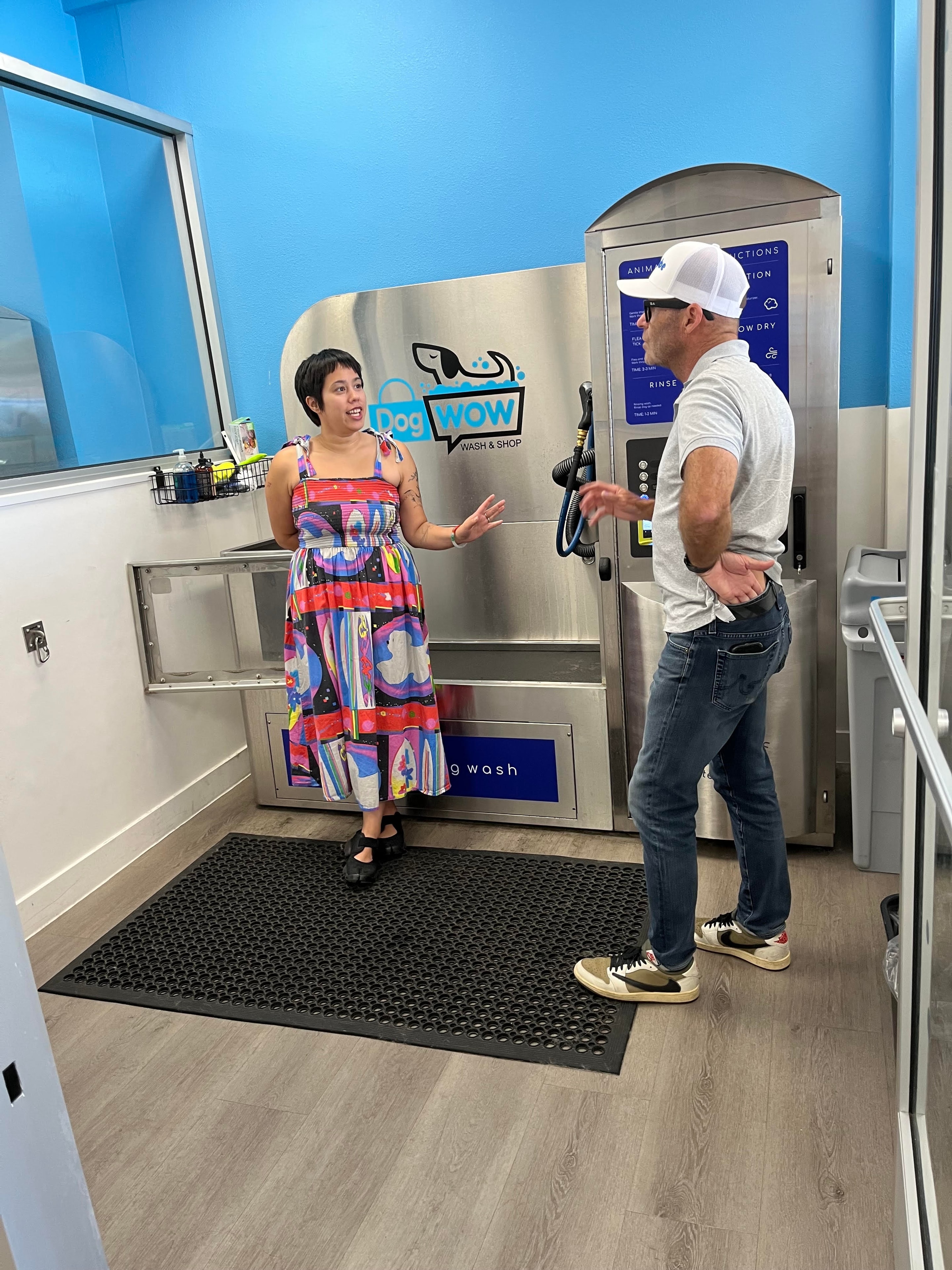 DOGWOW team member explaining the self-serve dog wash station to a customer inside the Huntington Beach location
